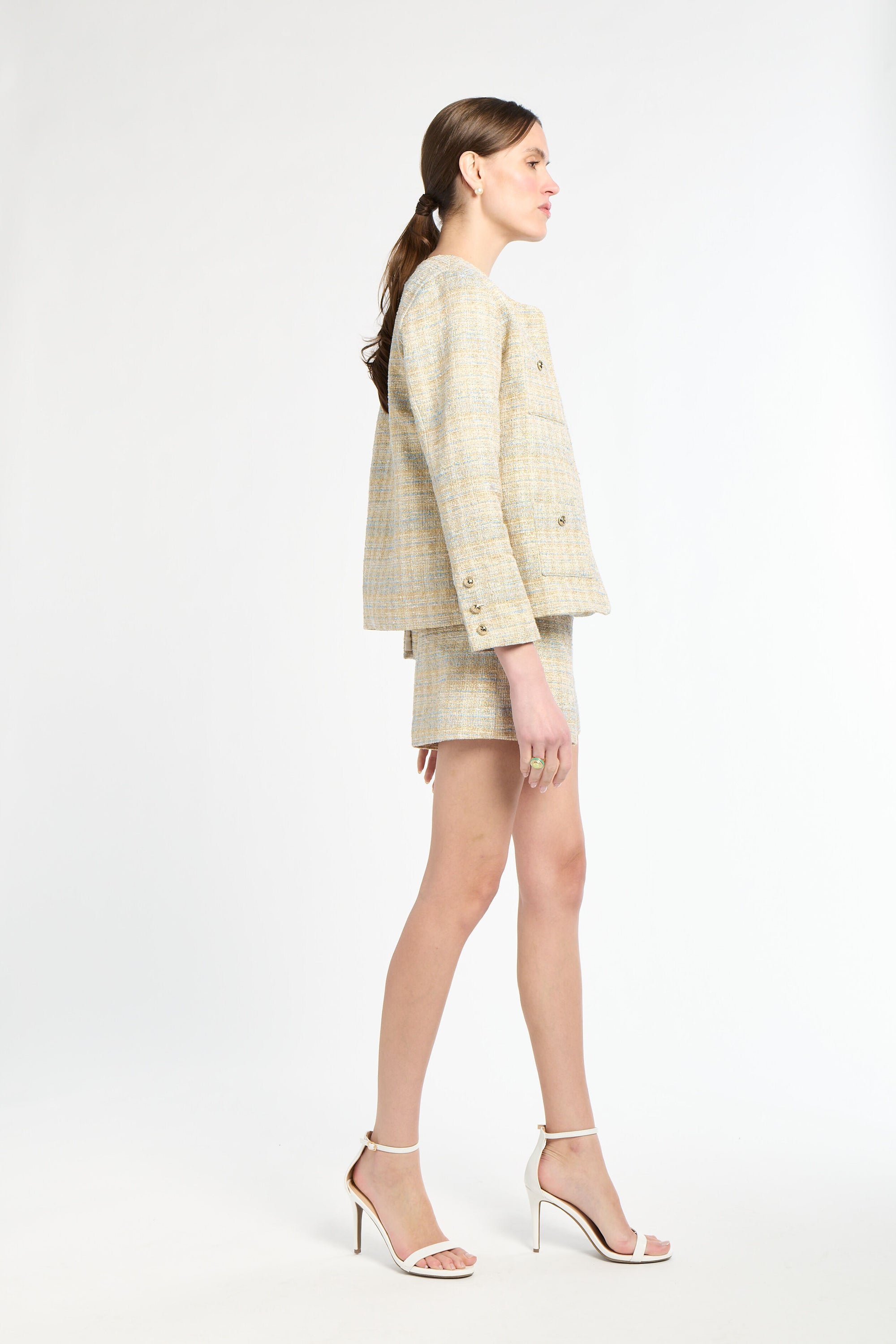 Side angle shot of woman wearing a gold and light blue blazer and shorts set on a white background
