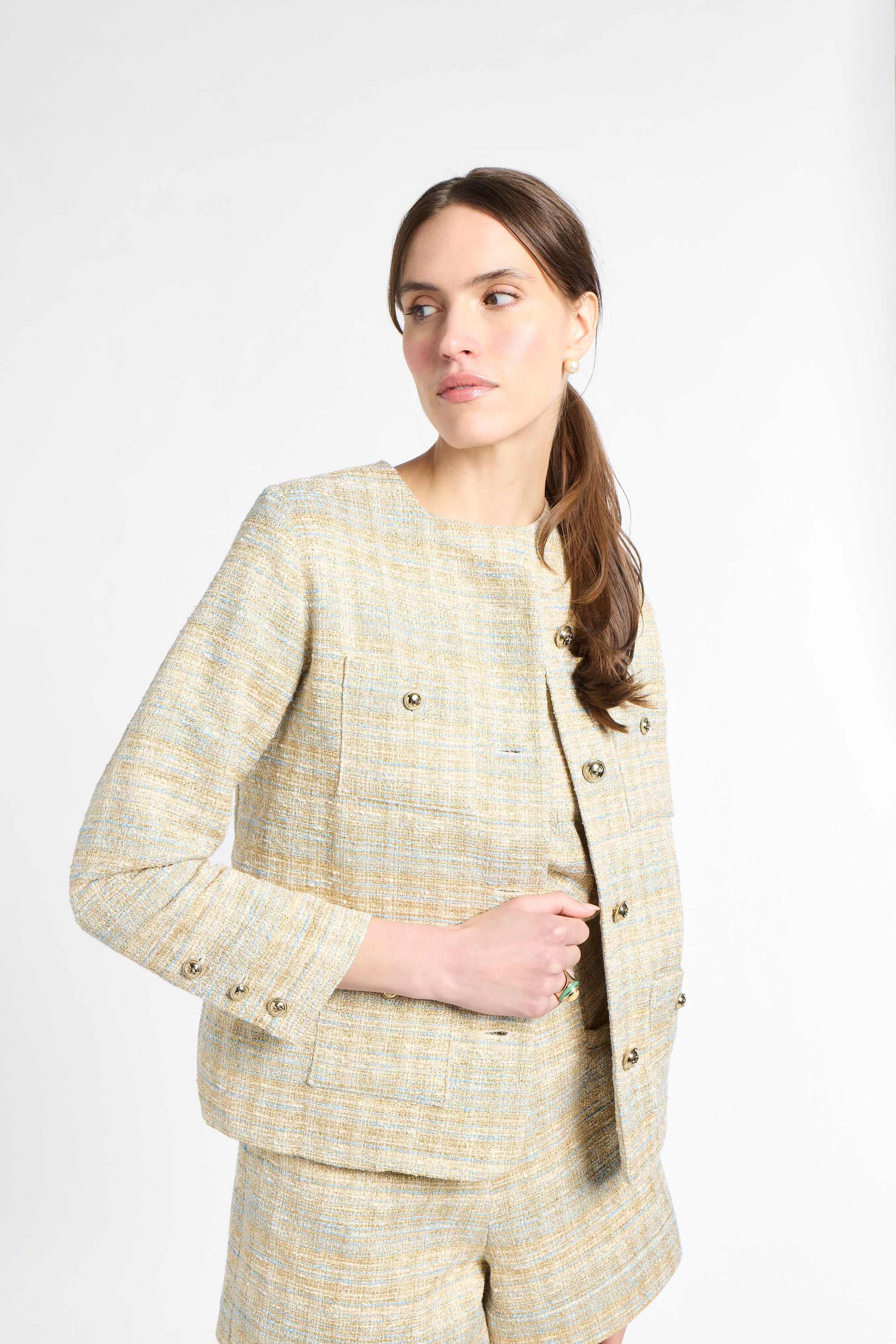 Woman wearing a golden and light blue blazer and shorts set on a white background