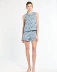 Woman wearing a sleeveless blue tweed top and shorts on a white background