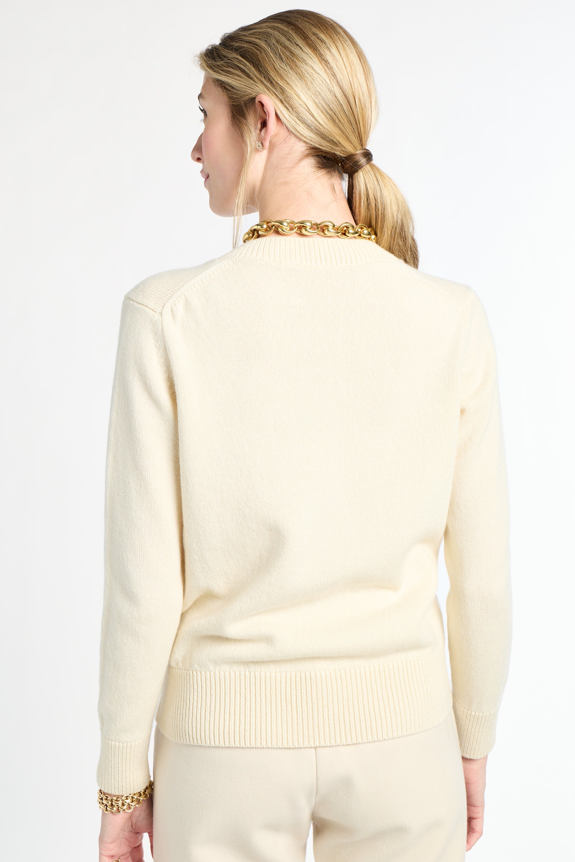 Woman wearing a light-colored sweater with a gold chain necklace on a white background