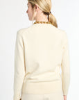 Woman wearing a light-colored sweater with a gold chain necklace on a white background