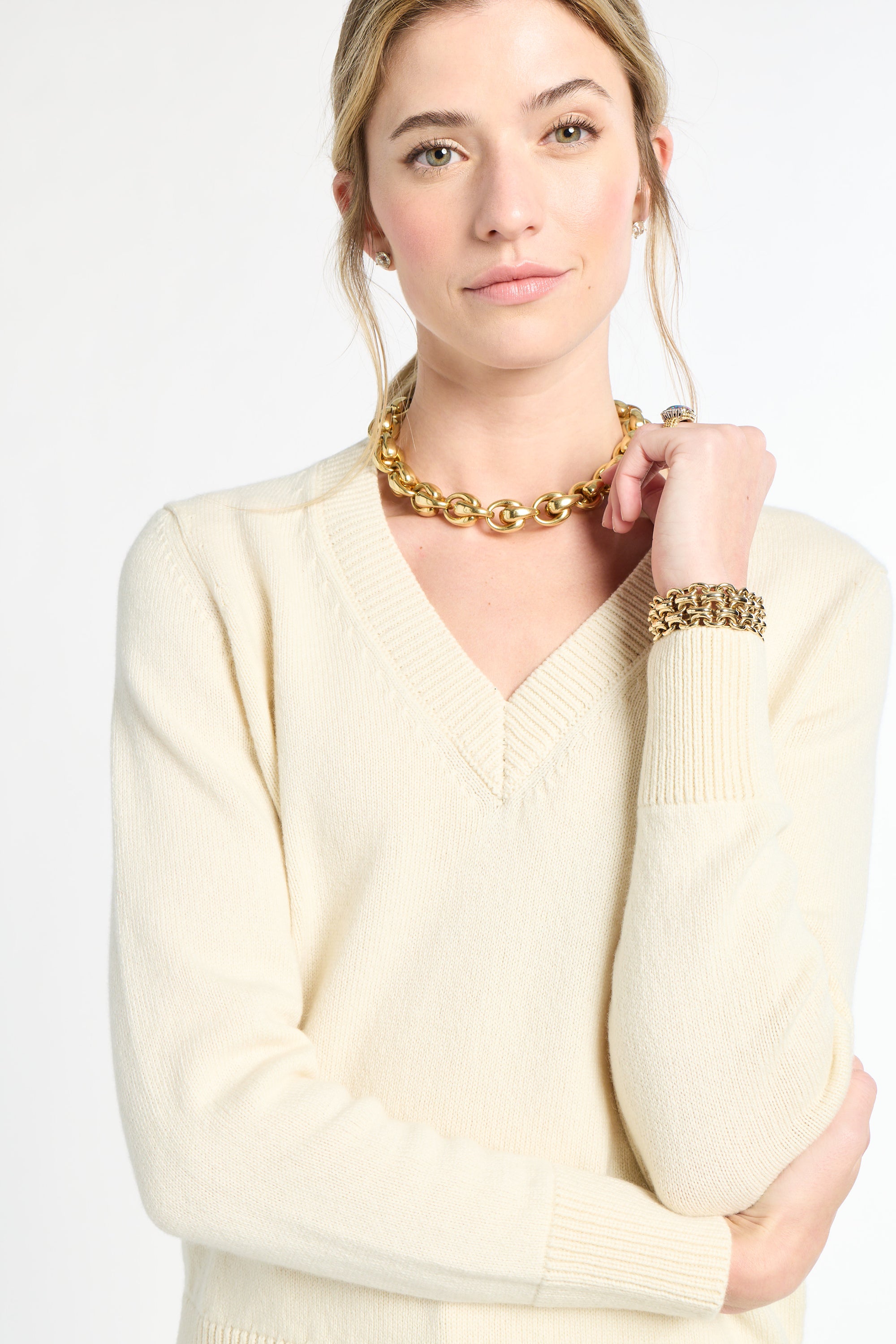 Woman wearing a cream sweater and gold jewelry on a white background