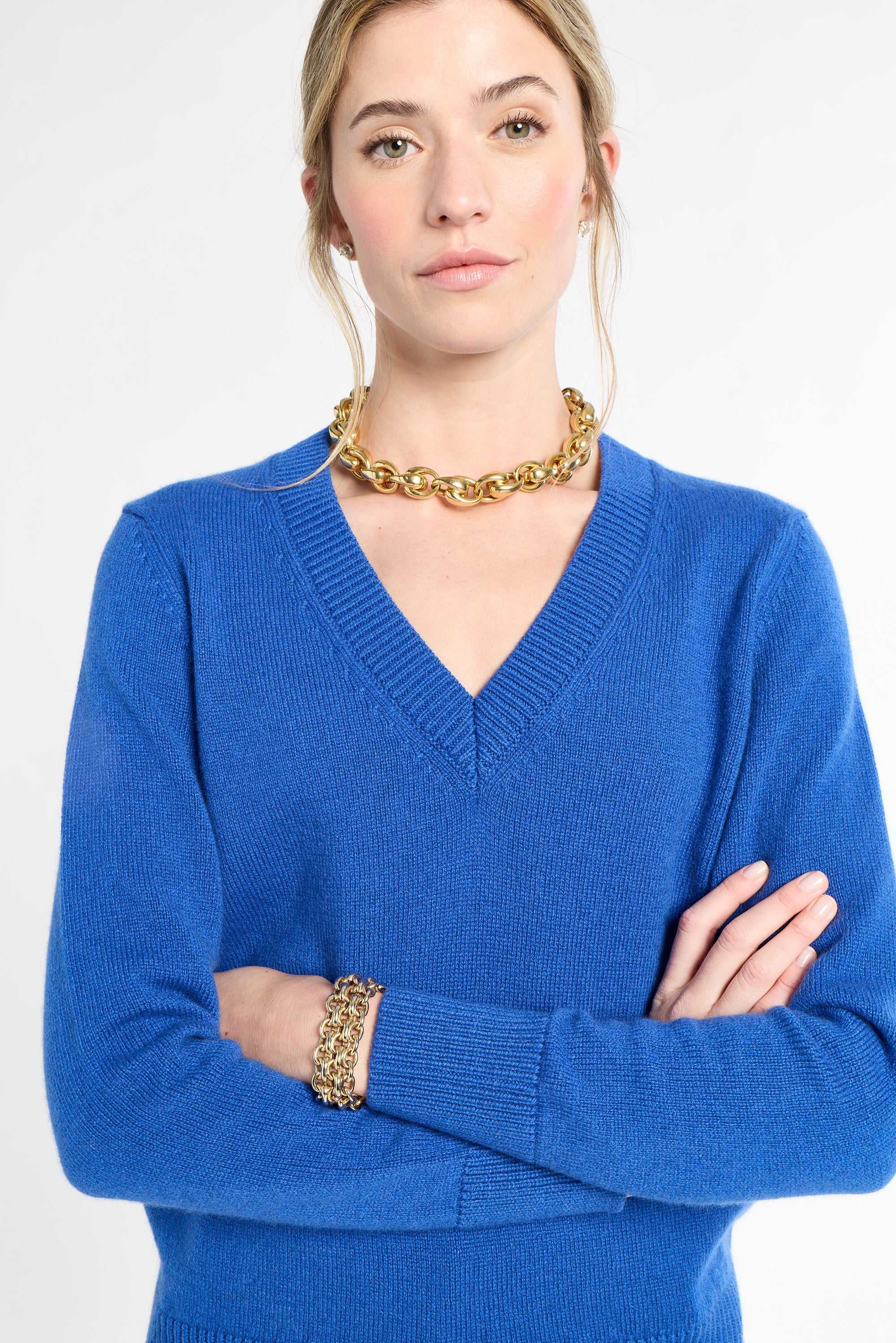 Woman wearing a blue sweater with gold jewelry on a white background
