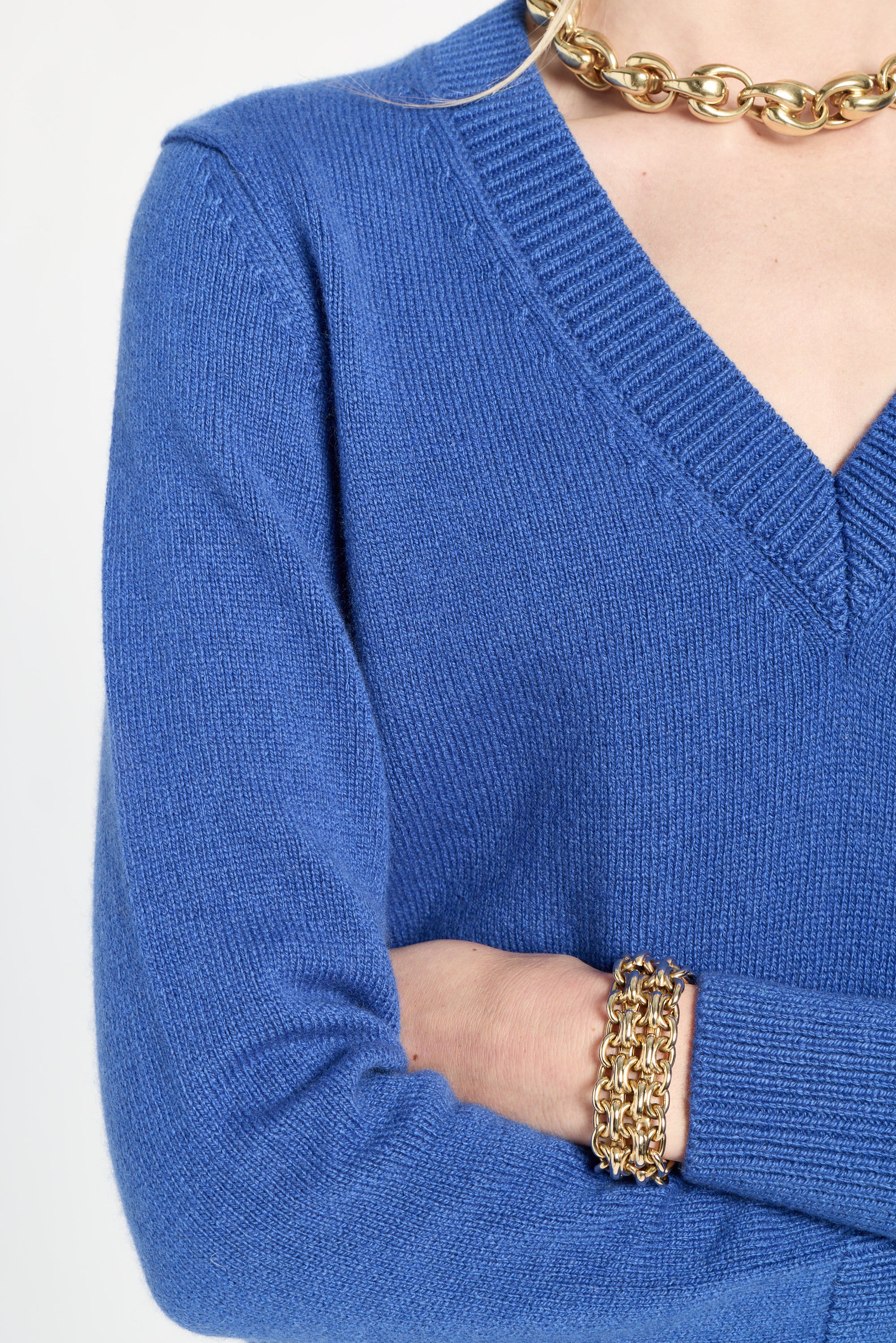 Blue sweater worn by a person with gold jewelry on a white background