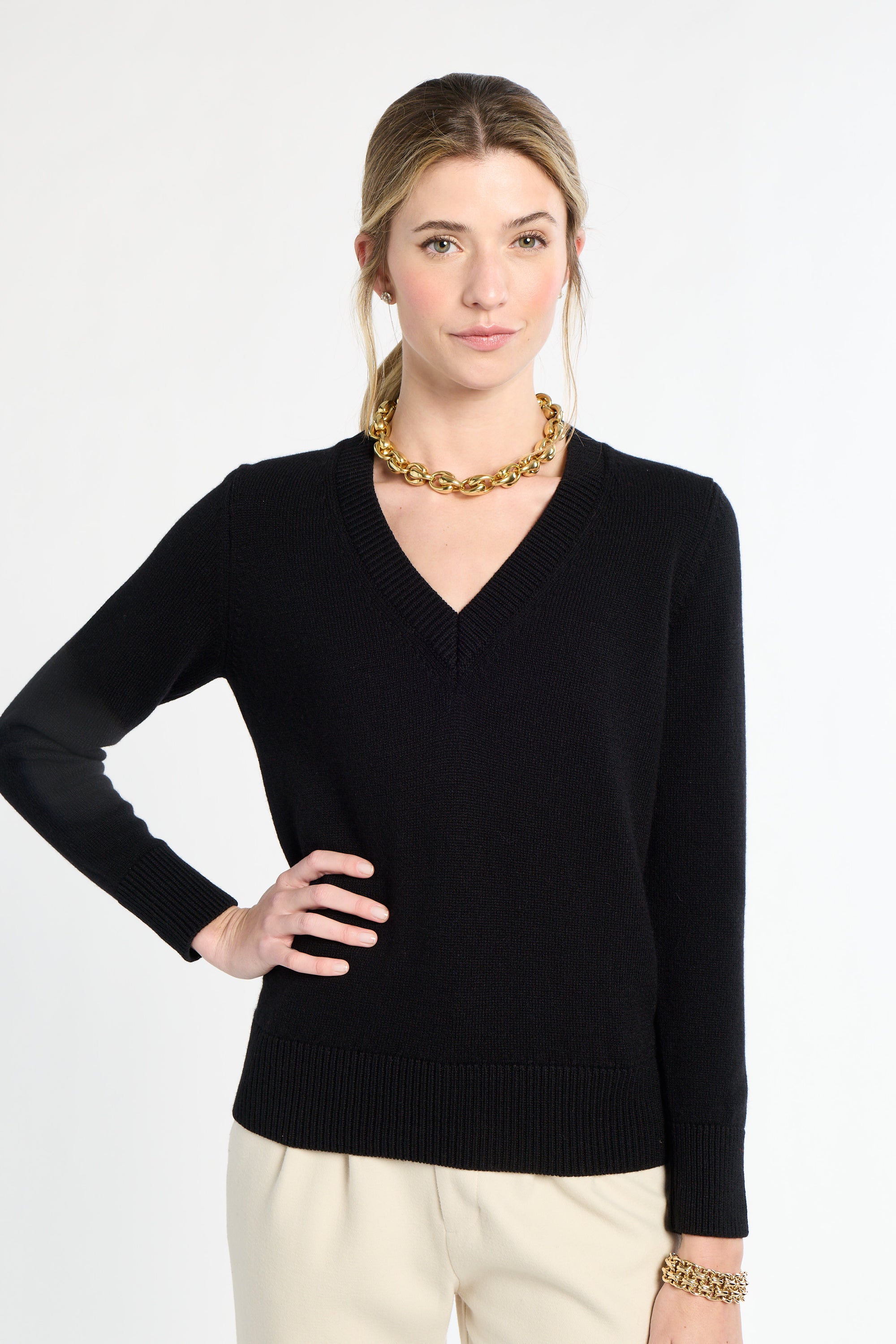Woman wearing a black sweater and gold necklace on a white background