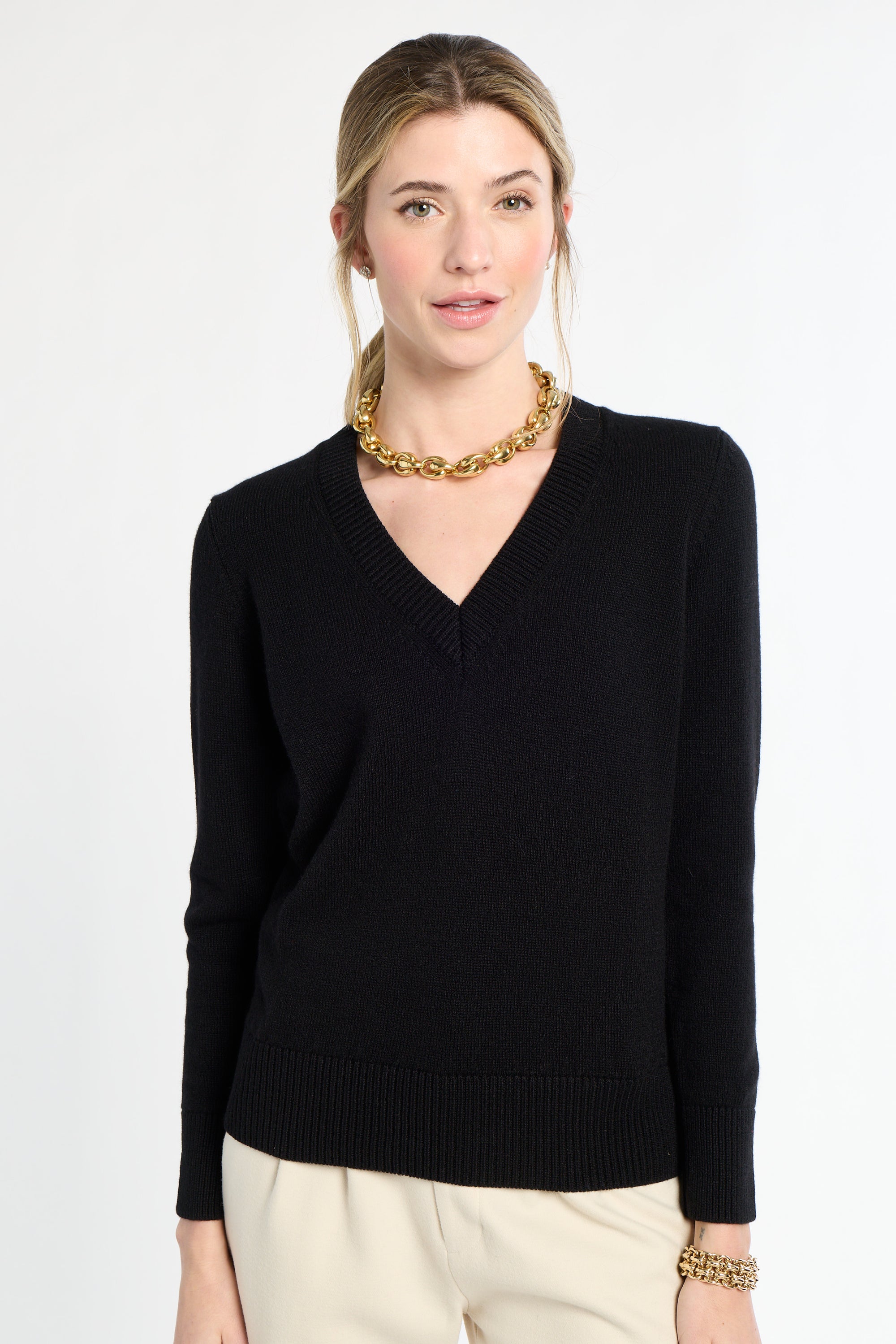Woman wearing a black sweater and gold necklace on a white background