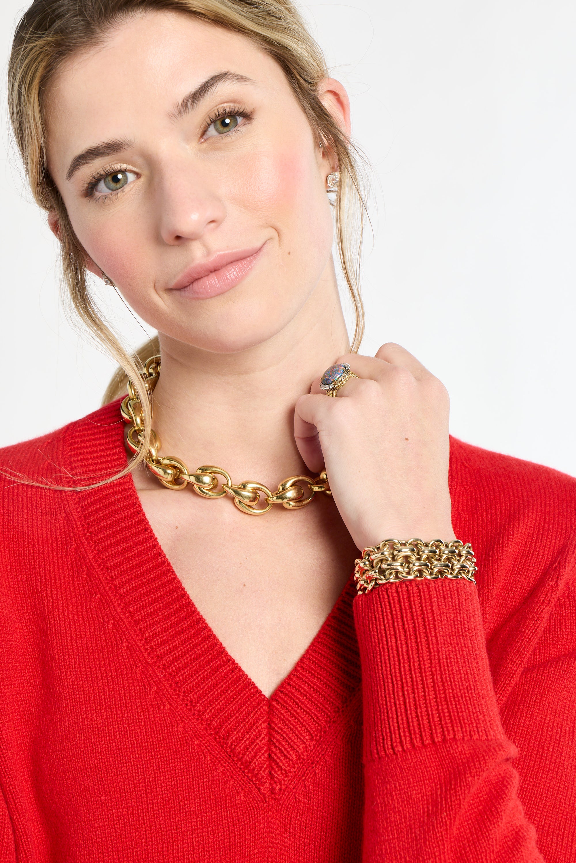 Woman wearing gold jewelry including a necklace, bracelet, and ring on a white background