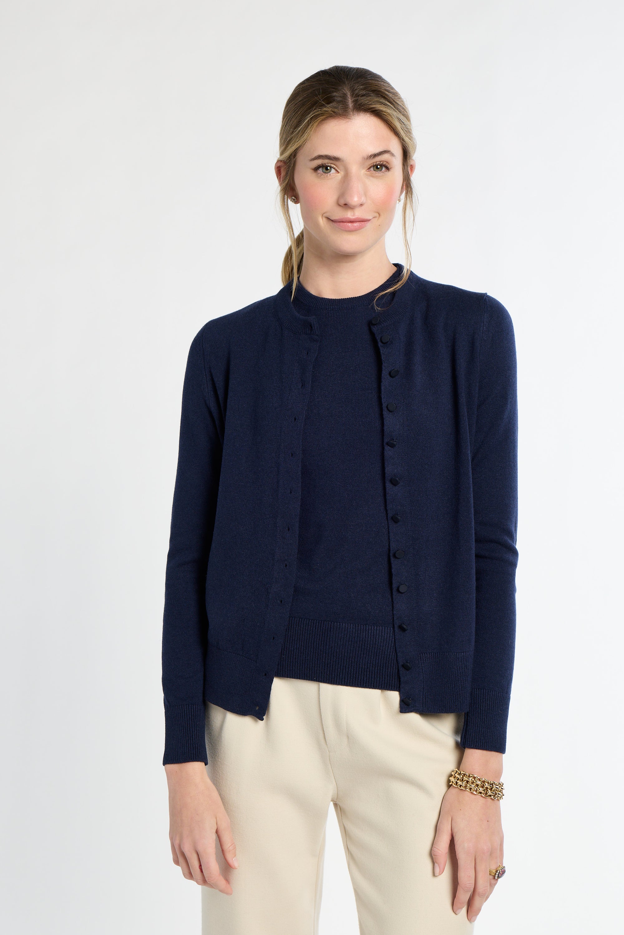 Woman wearing a navy cardigan over a black top with beige pants on a white background