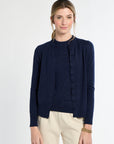 Woman wearing a navy cardigan over a black top with beige pants on a white background