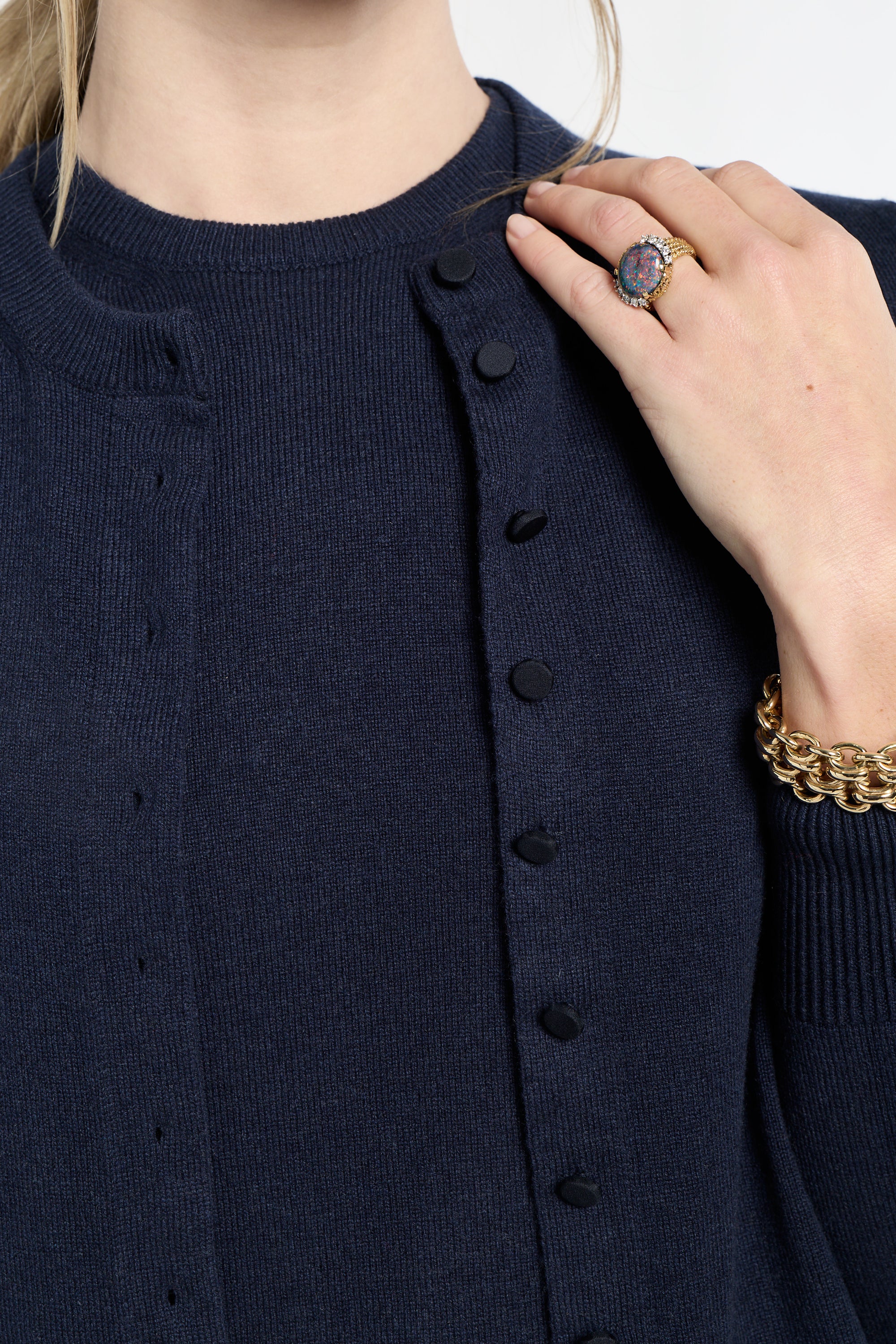 Navy blue cardigan with black buttons worn by a person, with a hand touching the fabric.