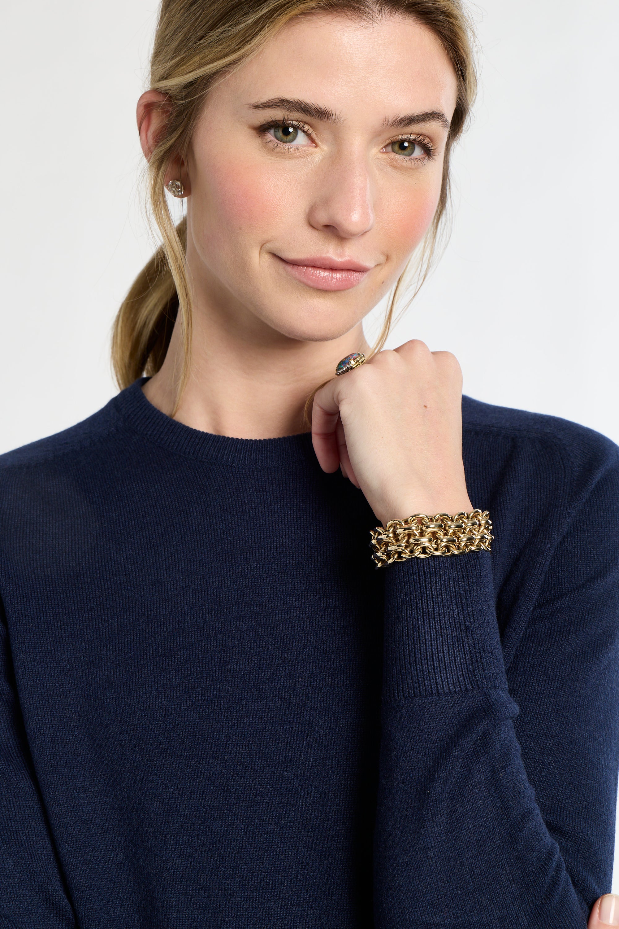Woman wearing a navy sweater with a gold bracelet on a white background
