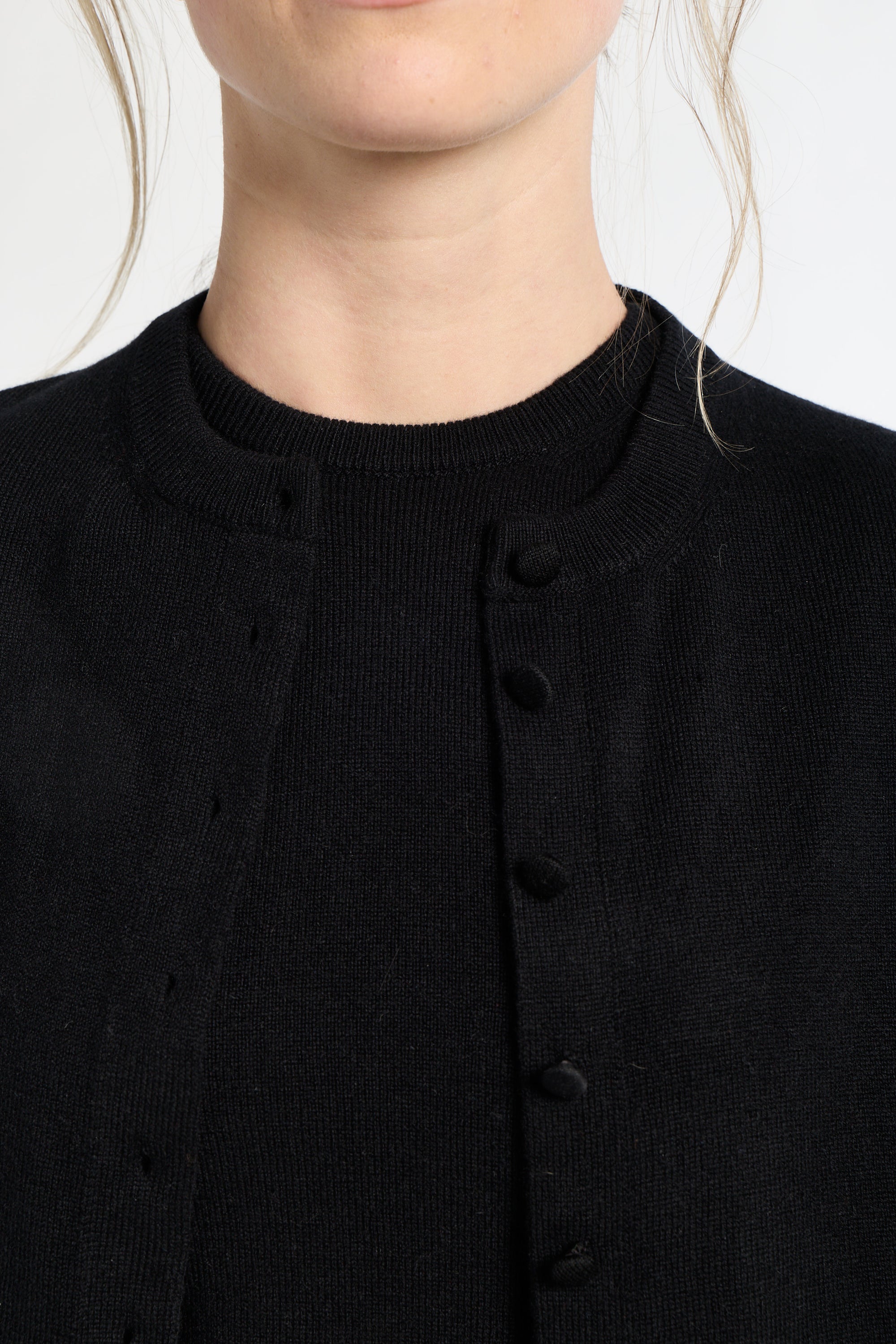 Close-up of a person wearing a black cardigan with buttons on a white background