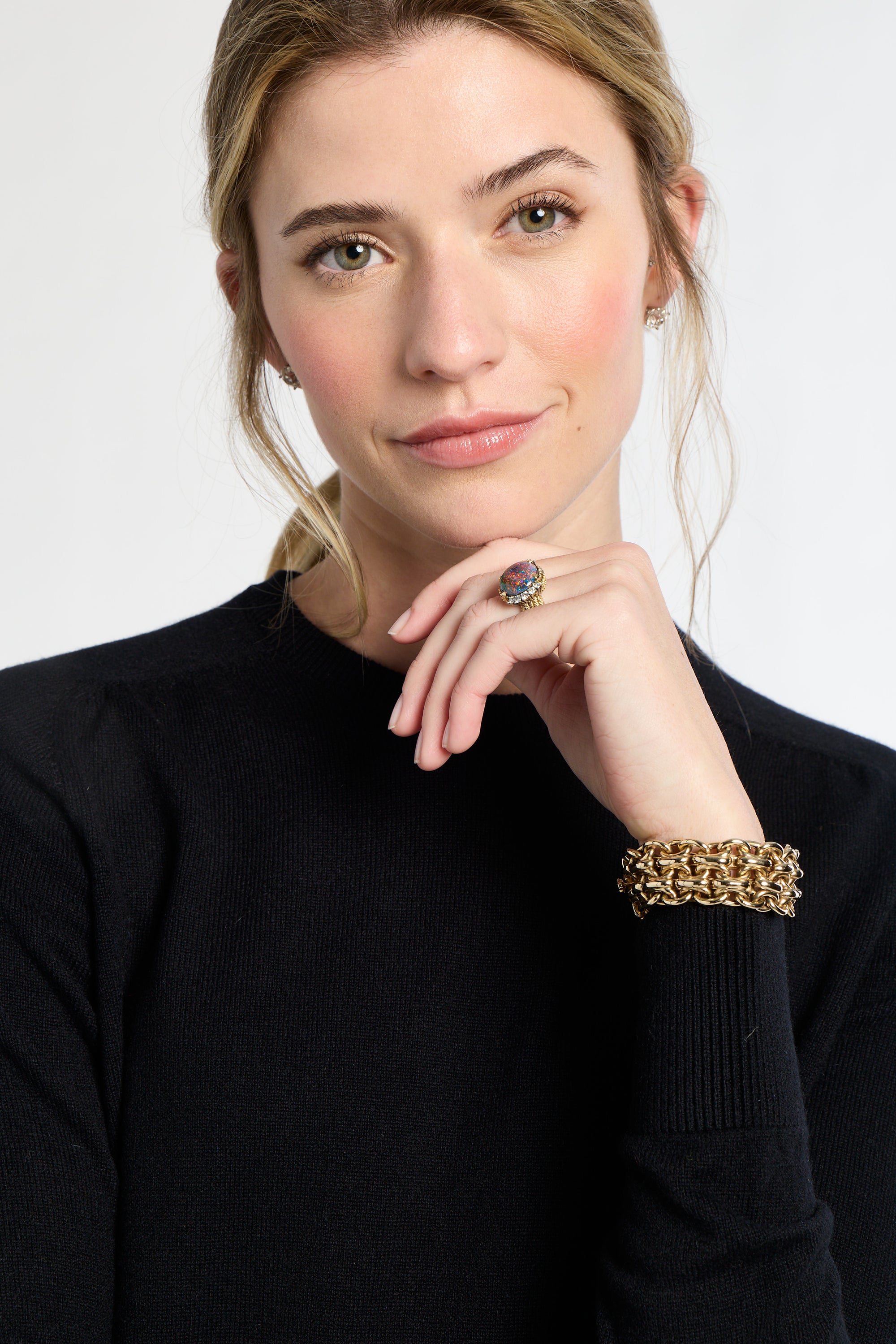 Woman wearing a black sweater with a gold bracelet and ring on a white background