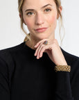 Woman wearing a black sweater with a gold bracelet and ring on a white background