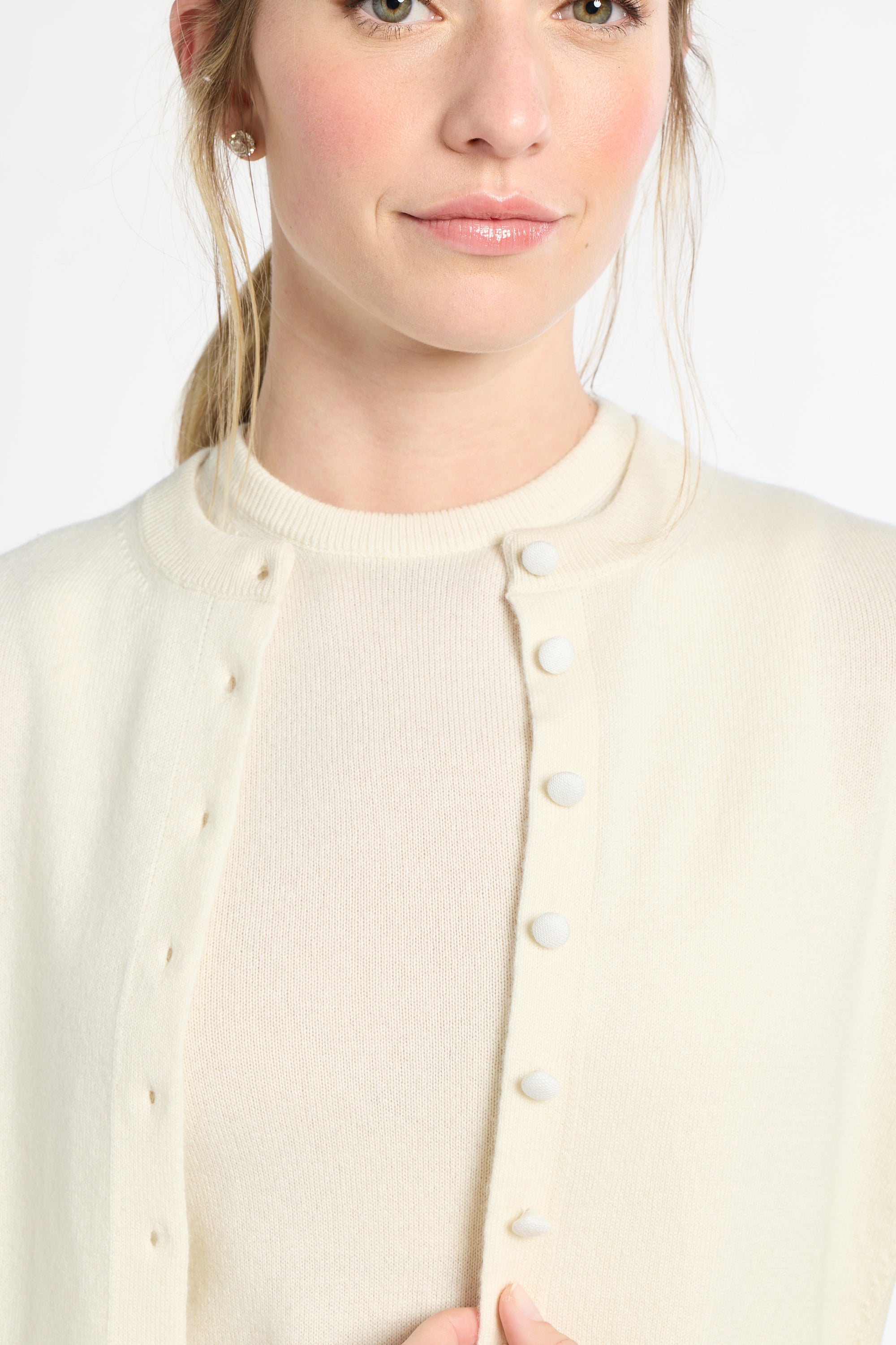 Close-up of a person wearing a cream-colored cardigan with buttons on a white background