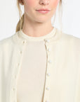 Close-up of a person wearing a cream-colored cardigan with buttons on a white background