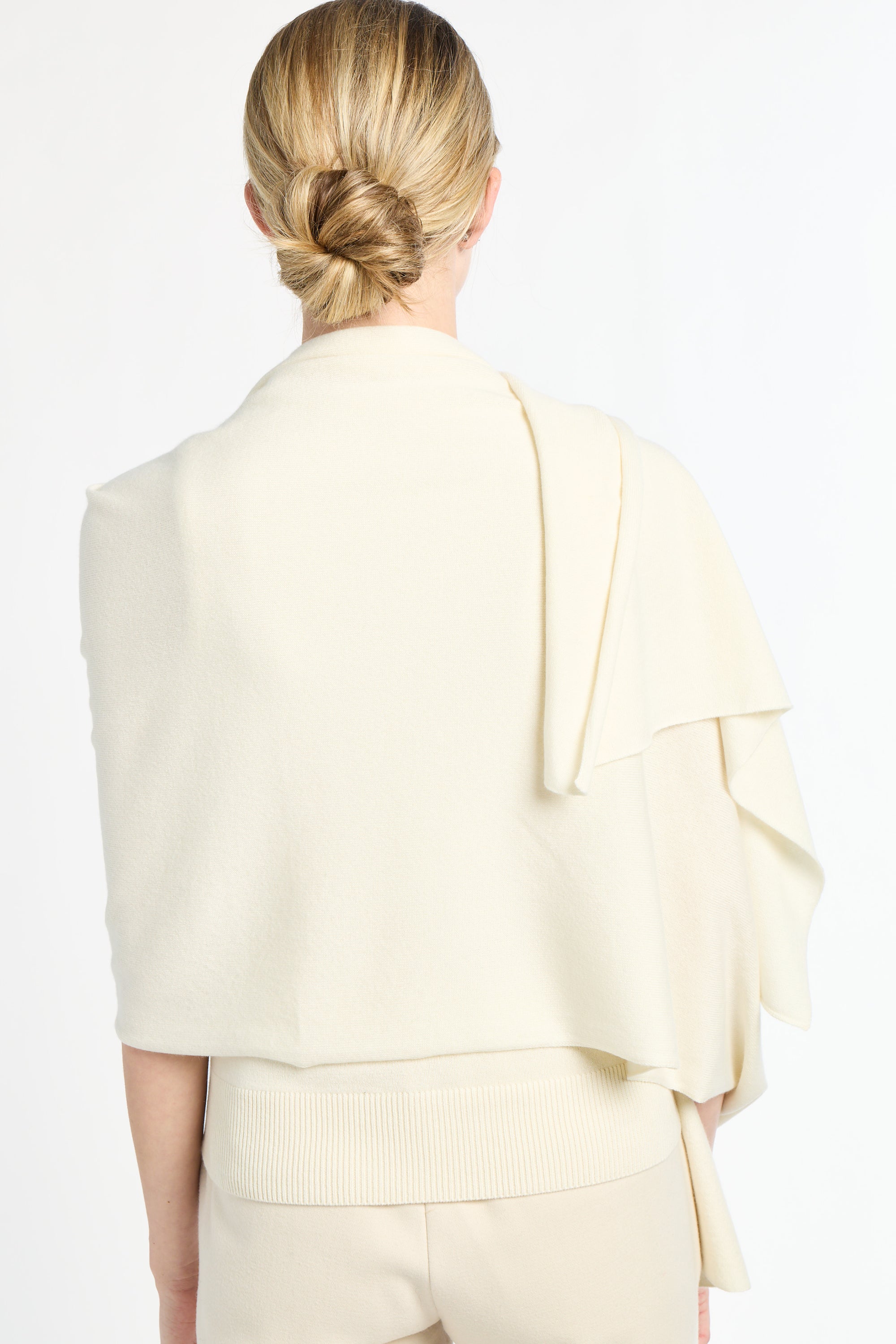 Person wearing a light-colored outfit with a draped design on a white background