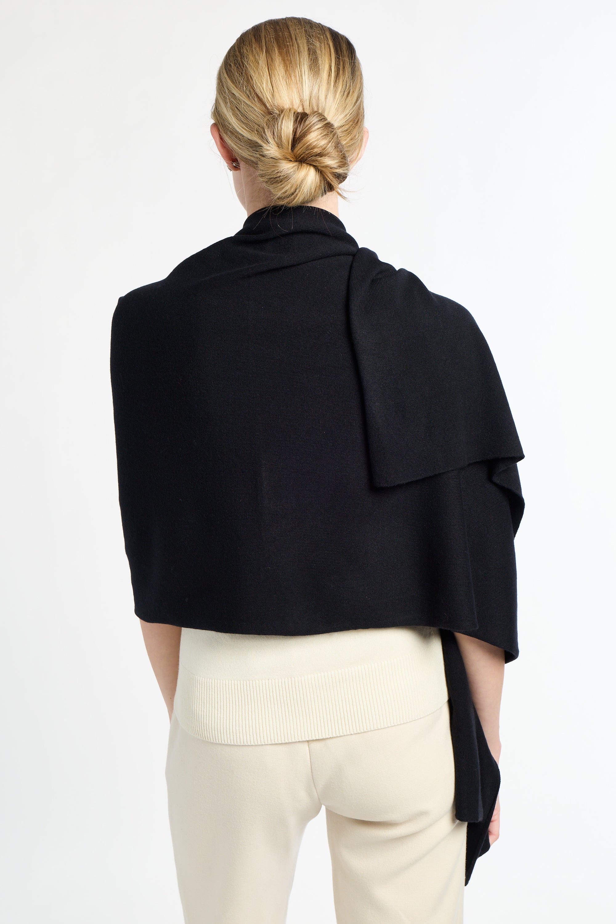 Person wearing a black drapey top over a white outfit on a plain background