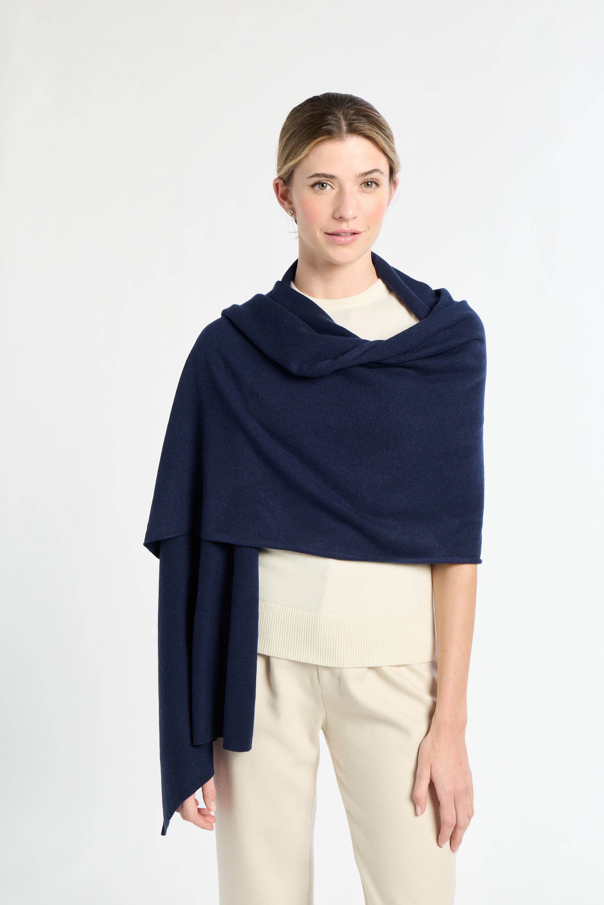 Woman wearing a navy blue shawl over a white top and beige pants on a light gray background