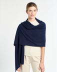 Woman wearing a navy blue shawl over a white top and beige pants on a light gray background