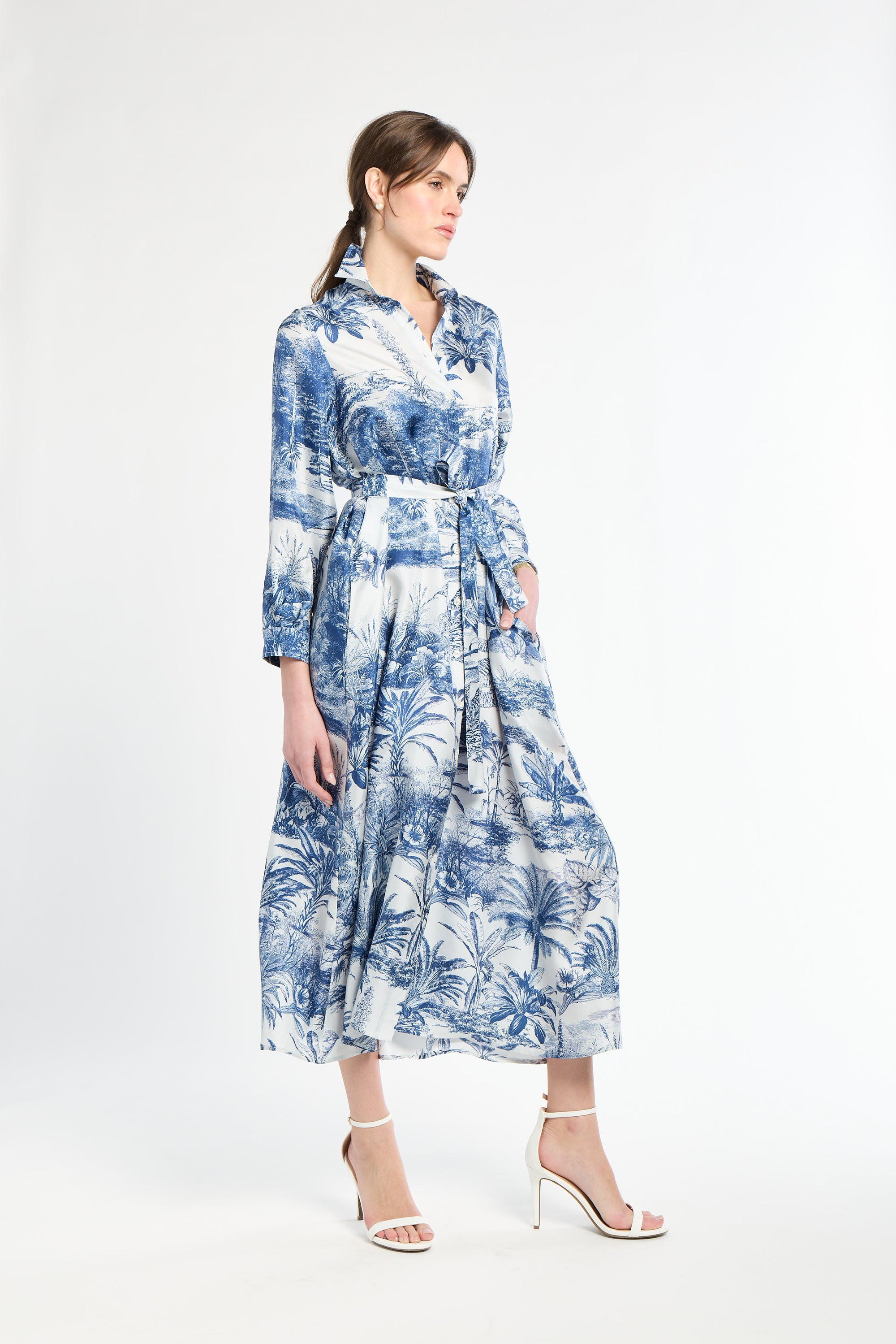 Woman wearing a blue and white patterned dress and white heels on a white background