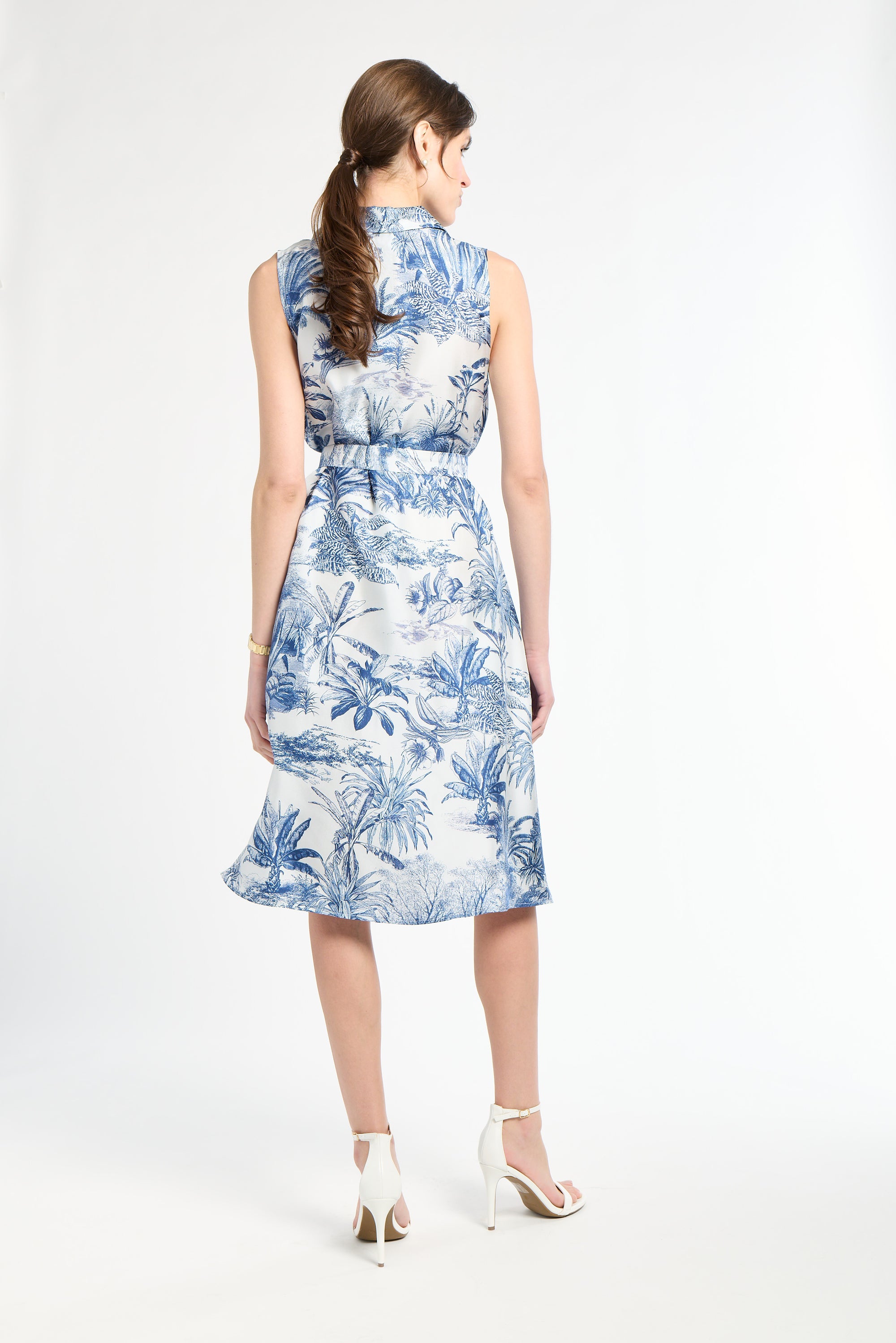 woman standing modeling a blue patterned dress with white heels on a white background