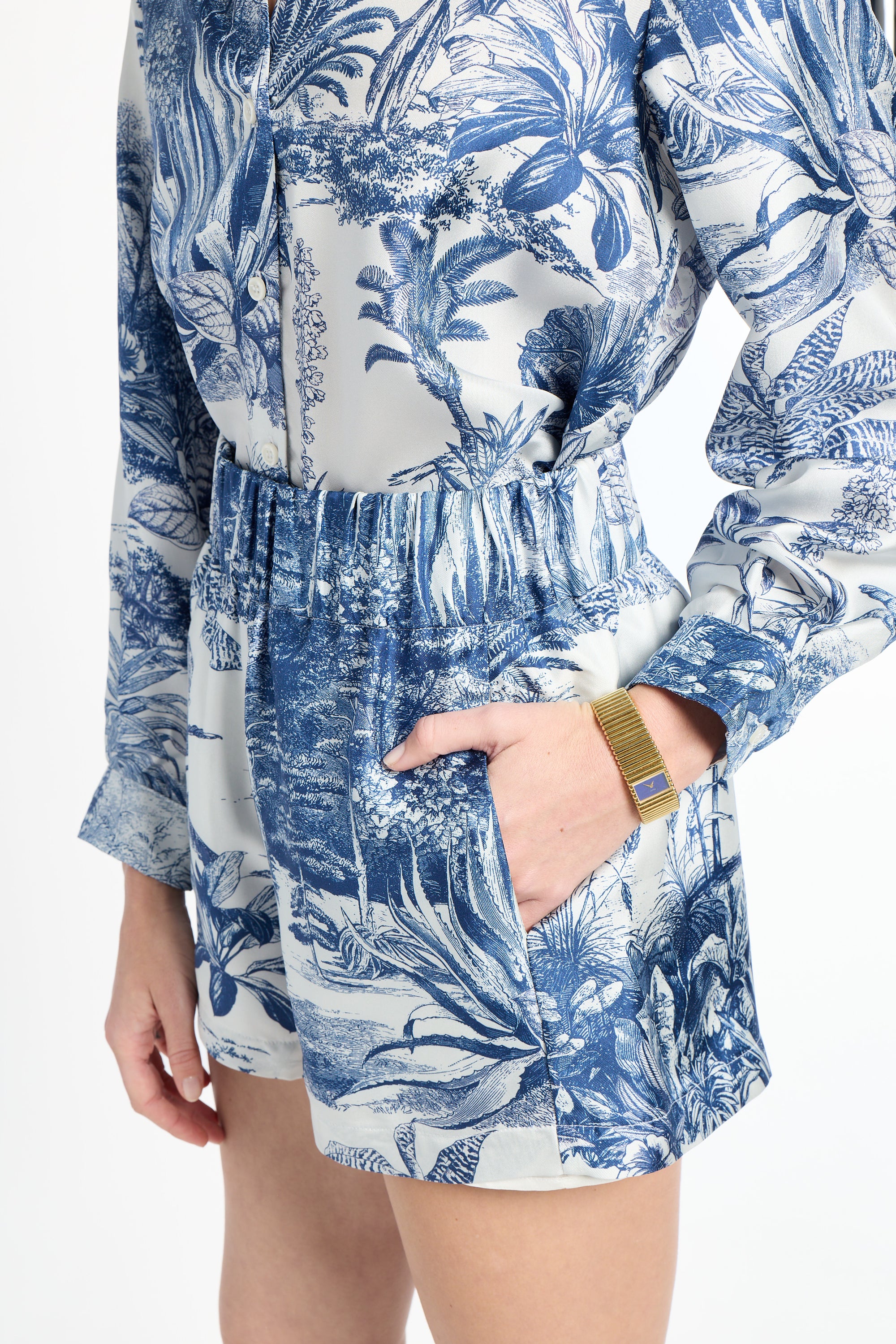 Woman with hand in her pocket modeling blue patterned shorts on a white background