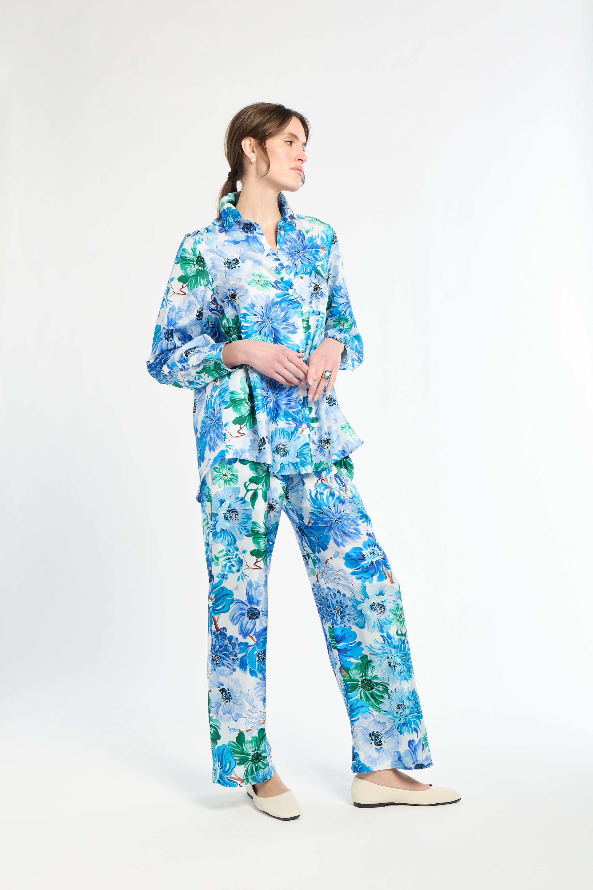 Side angle of woman wearing a blue and green floral shirt with matching pants on a white background