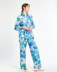 Side angle of woman wearing a blue and green floral shirt with matching pants on a white background
