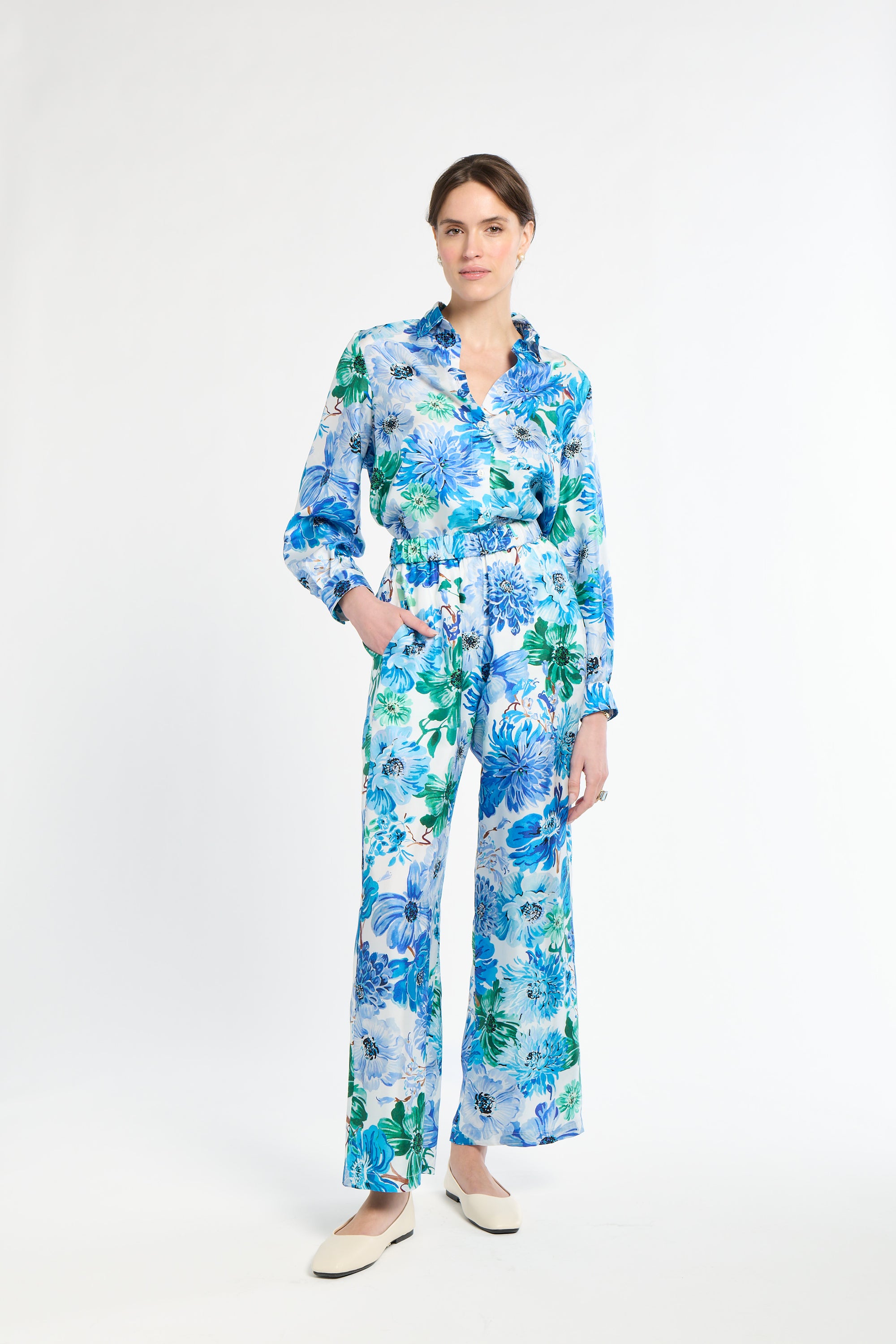 Woman wearing a tucked in blue and green floral shirt with matching pants on a white background