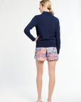 Woman wearing a navy sweater and colorful floral shorts on a white background