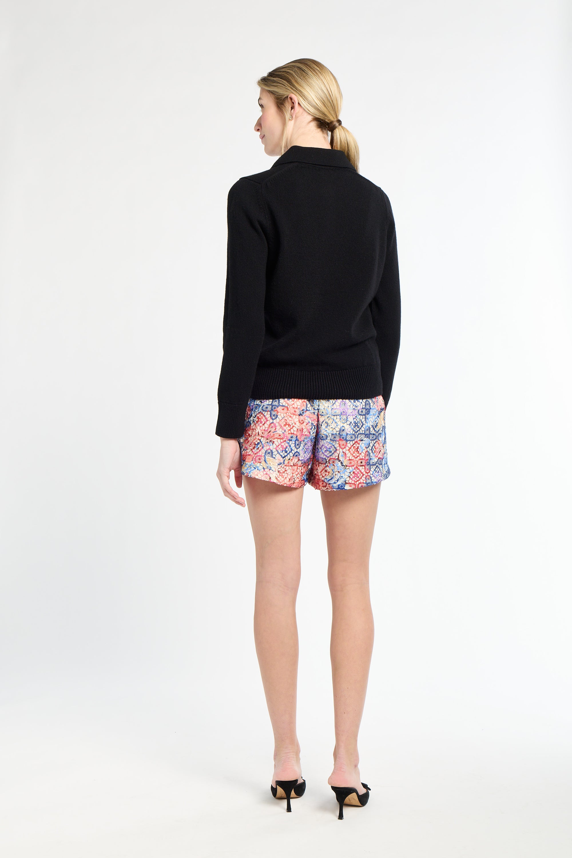 Woman wearing a black sweater and colorful floral shorts on a white background