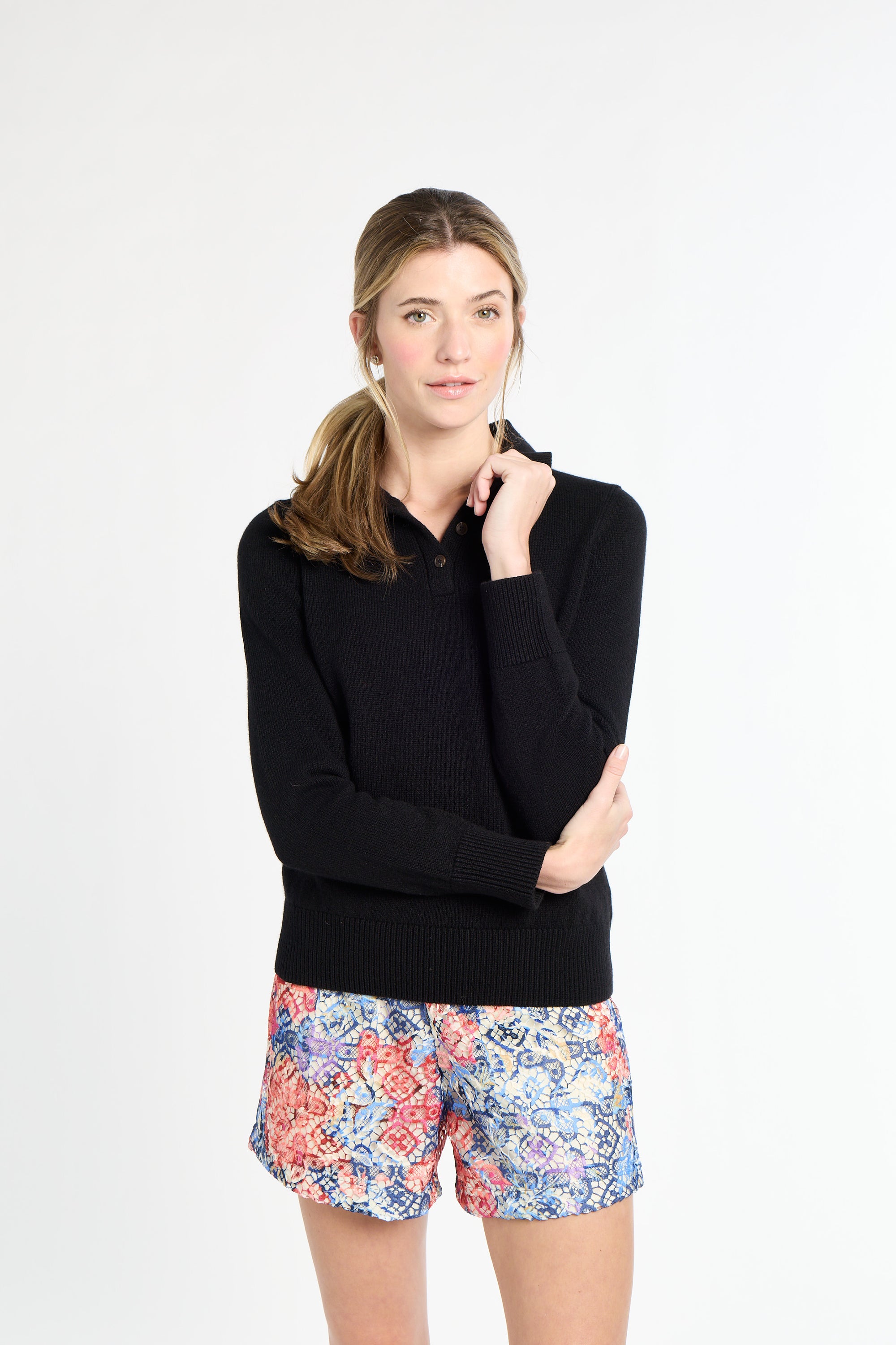 Woman wearing a black long-sleeve top and colorful floral shorts on a white background