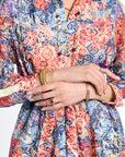 Close-up of a person wearing a colorful floral dress with hands clasped together.