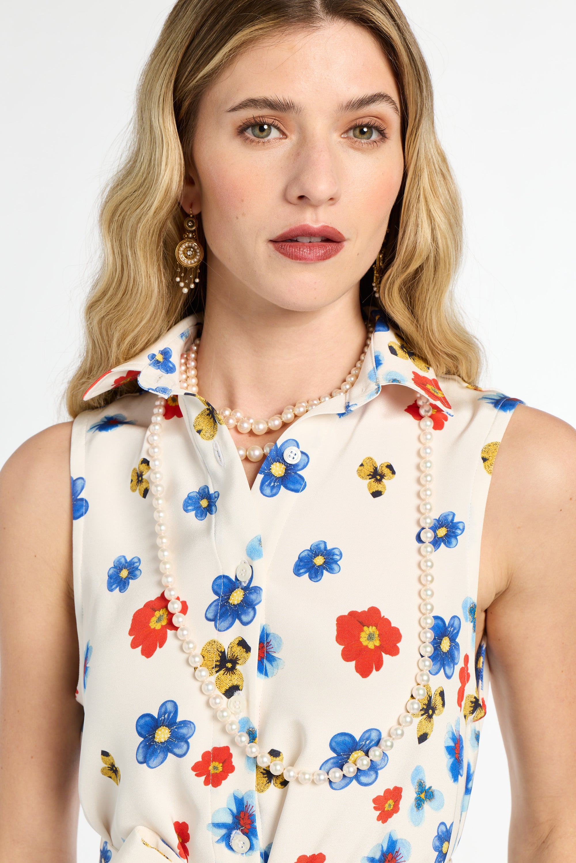 Woman wearing a sleeveless blouse with colorful floral pattern and pearl necklace on a white background
