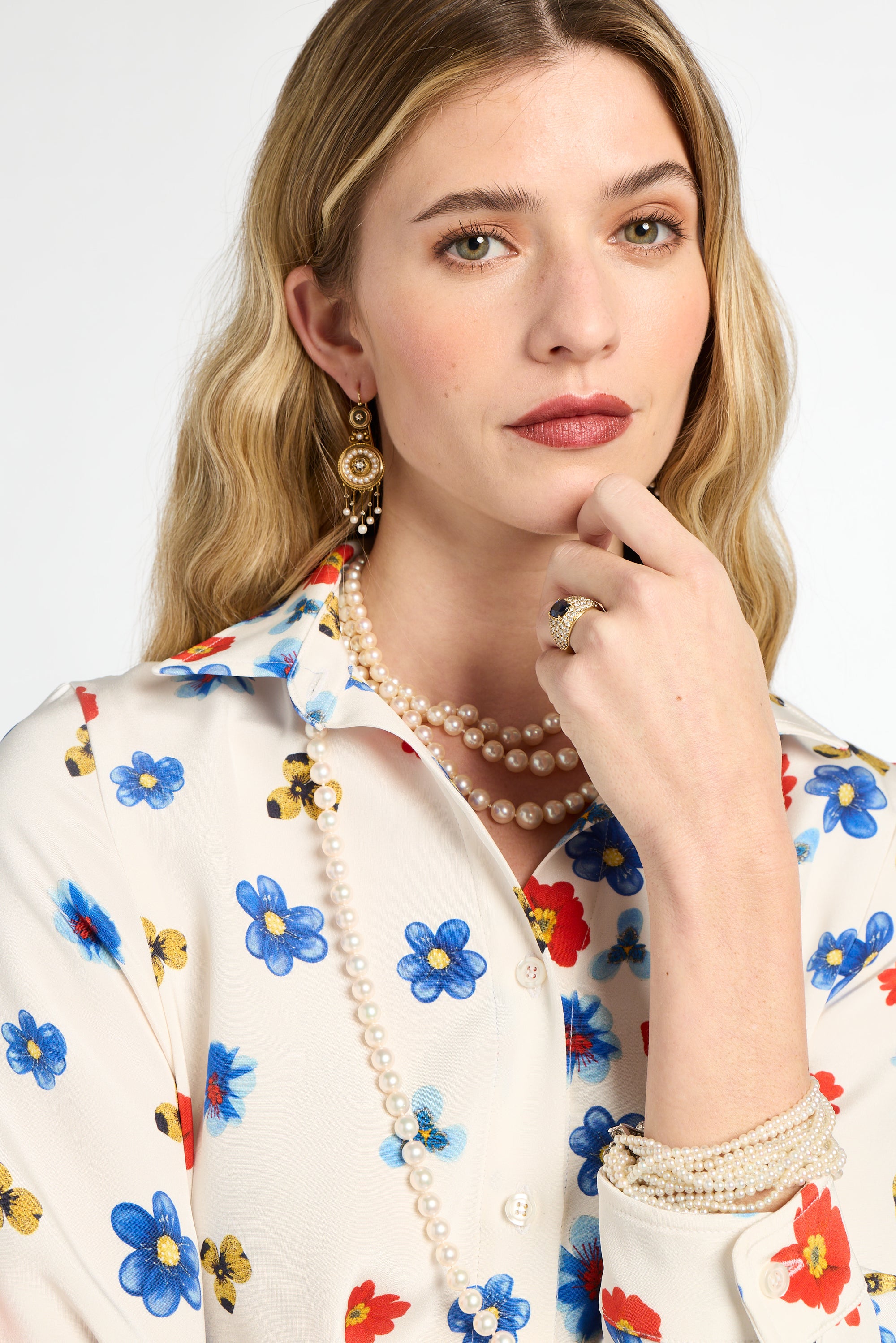 Woman wearing a floral blouse with a pearl necklace and earrings against a white background