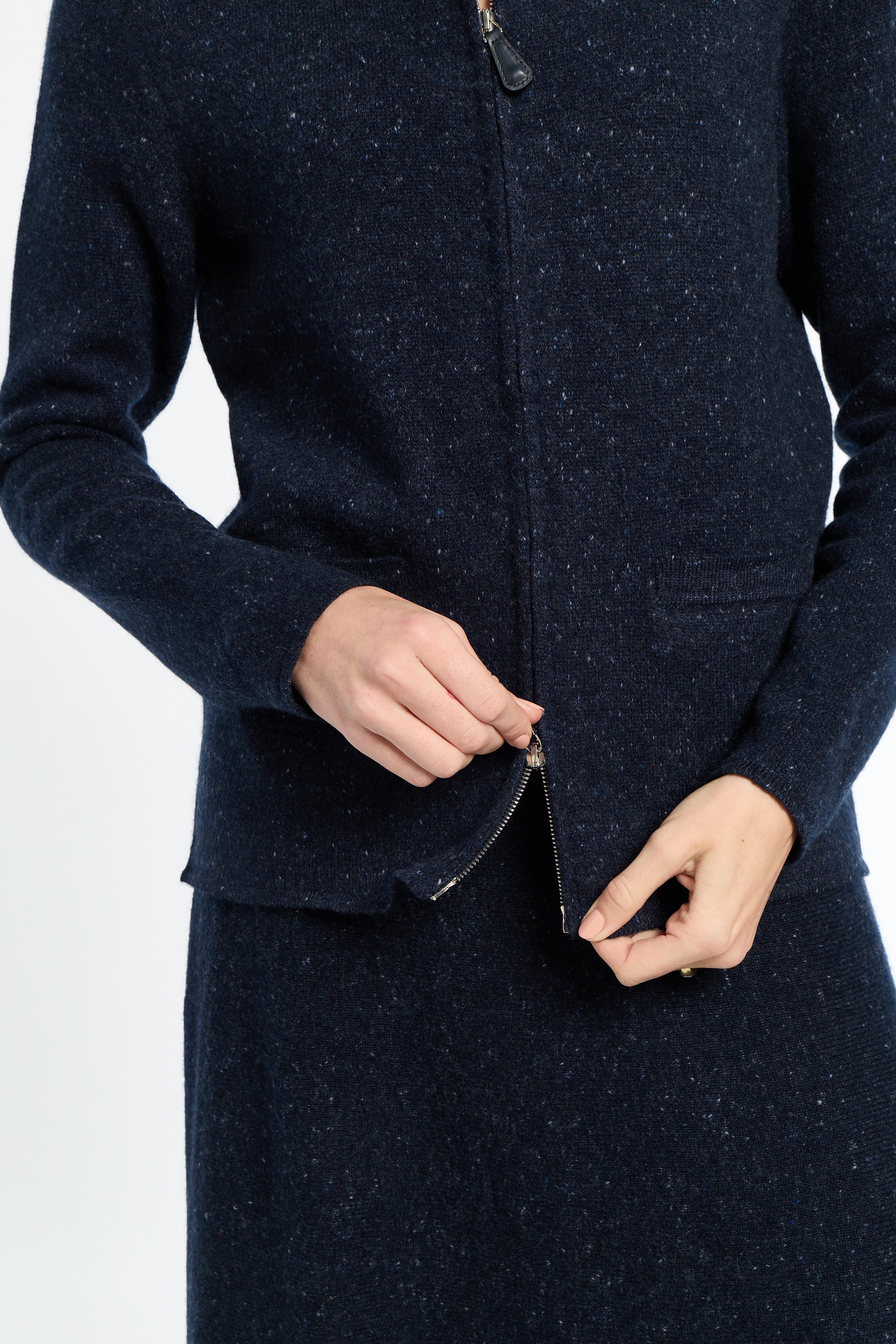Navy blue coat with a close-up of a hand zipping it up on a white background