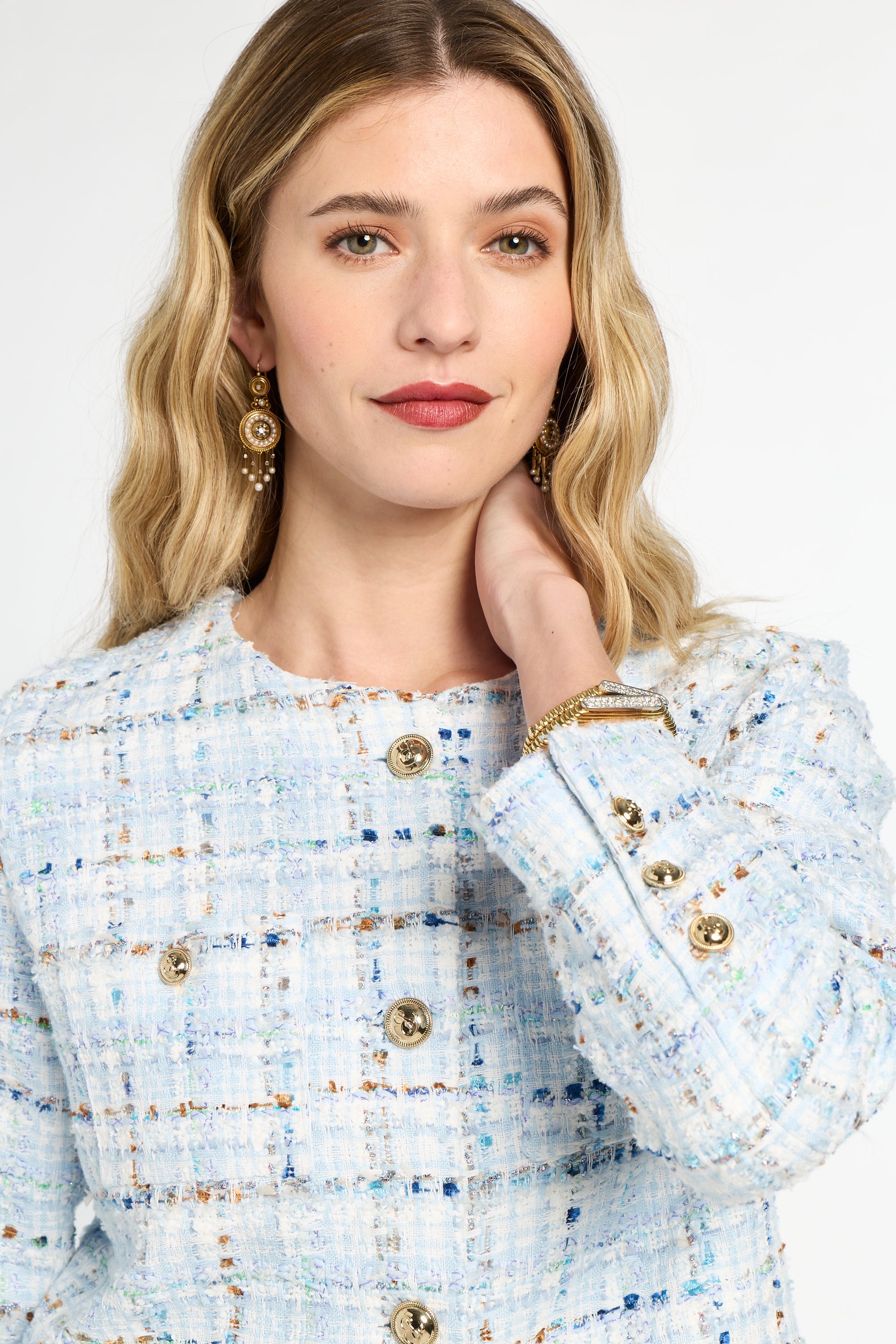 Woman wearing a light blue tweed jacket with gold buttons on a white background