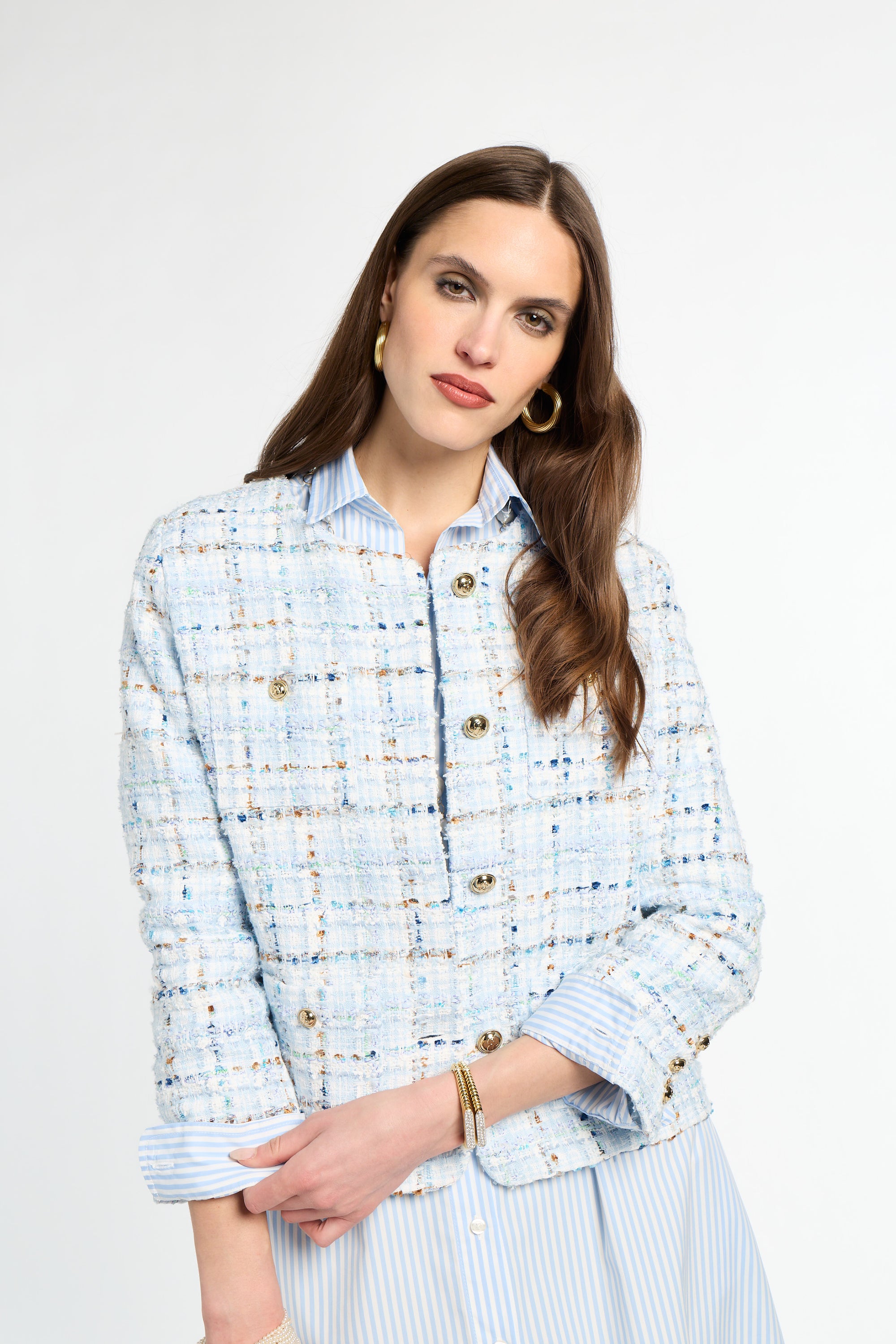 Woman wearing a light blue tweed jacket with gold buttons on a white background