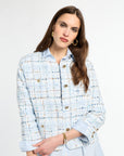 Woman wearing a light blue tweed jacket with gold buttons on a white background