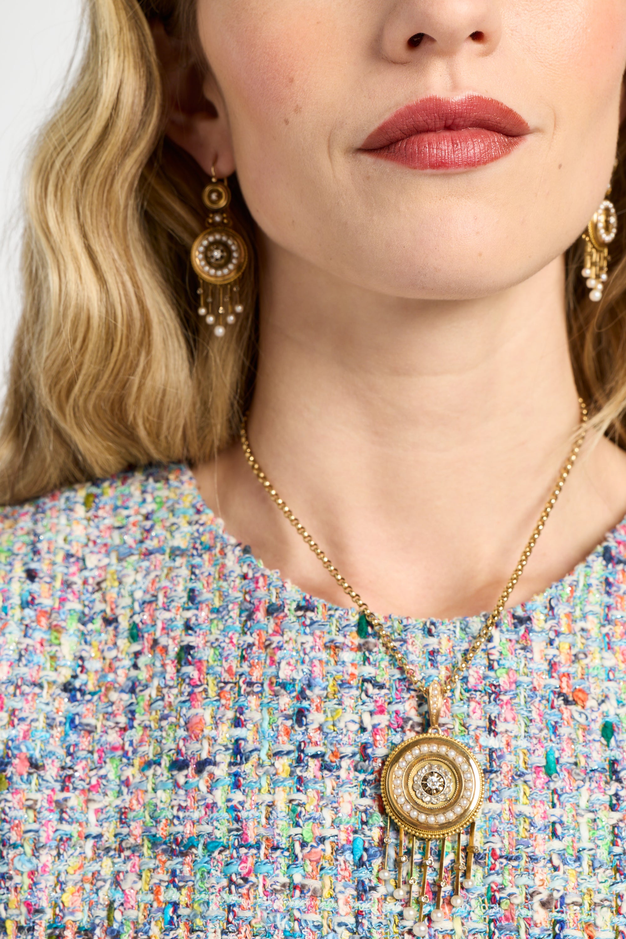 Close-up of a woman wearing a gold necklace with a pendant, earrings, and multicolored top.