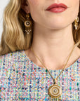 Close-up of a woman wearing a gold necklace with a pendant, earrings, and multicolored top.