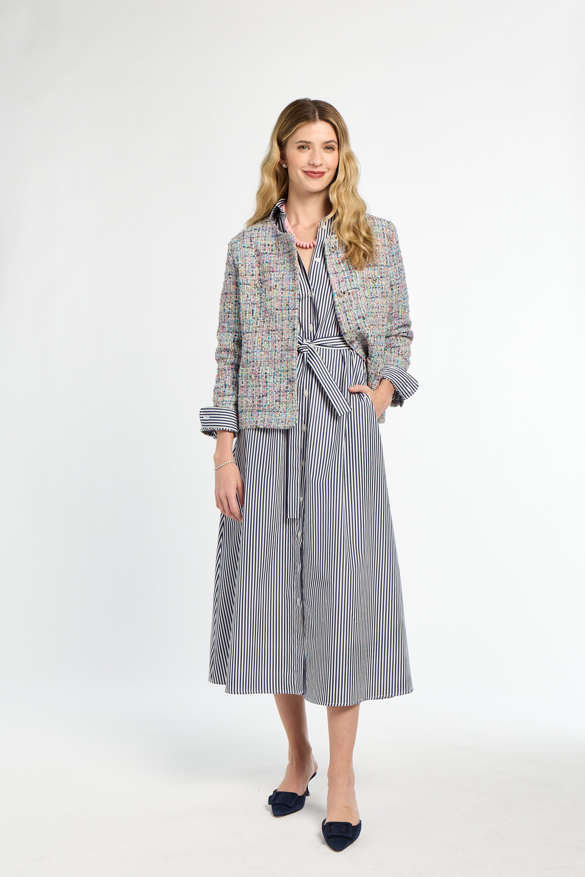 Woman wearing a tweed jacket over a striped dress on a white background