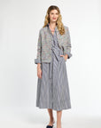 Woman wearing a tweed jacket over a striped dress on a white background