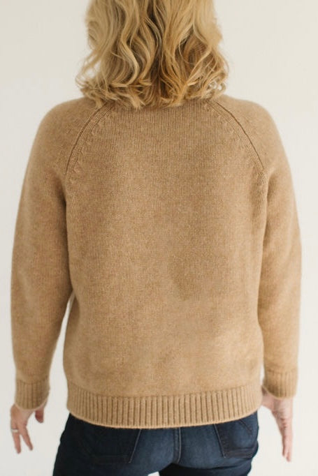 Back view of Eleanor Leftwich wearing the Boyfriend Turtleneck sweater in Camel, paired with dark jeans, against a white background.