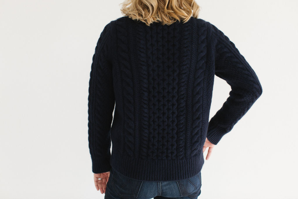 Back view of Eleanor Leftwich wearing the cable knit Fisherman Crewneck in navy, paired with dark jeans, standing against a white background.