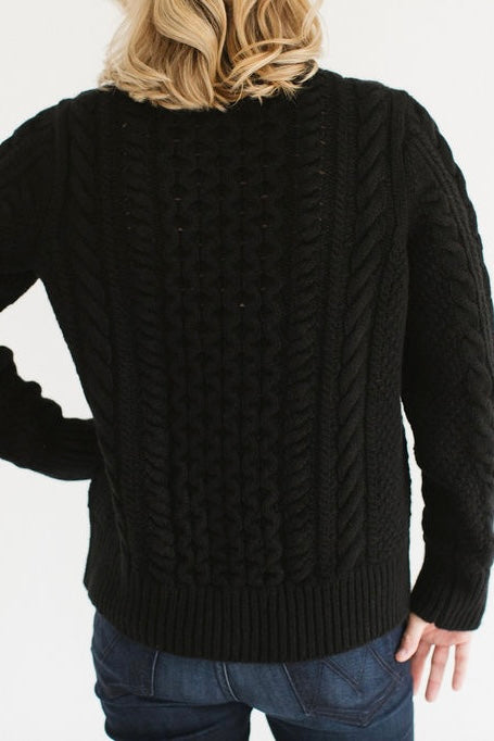 Back view of Eleanor Leftwich wearing the cable knit Fisherman Crewneck in Black, paired with dark jeans, standing against a white background.