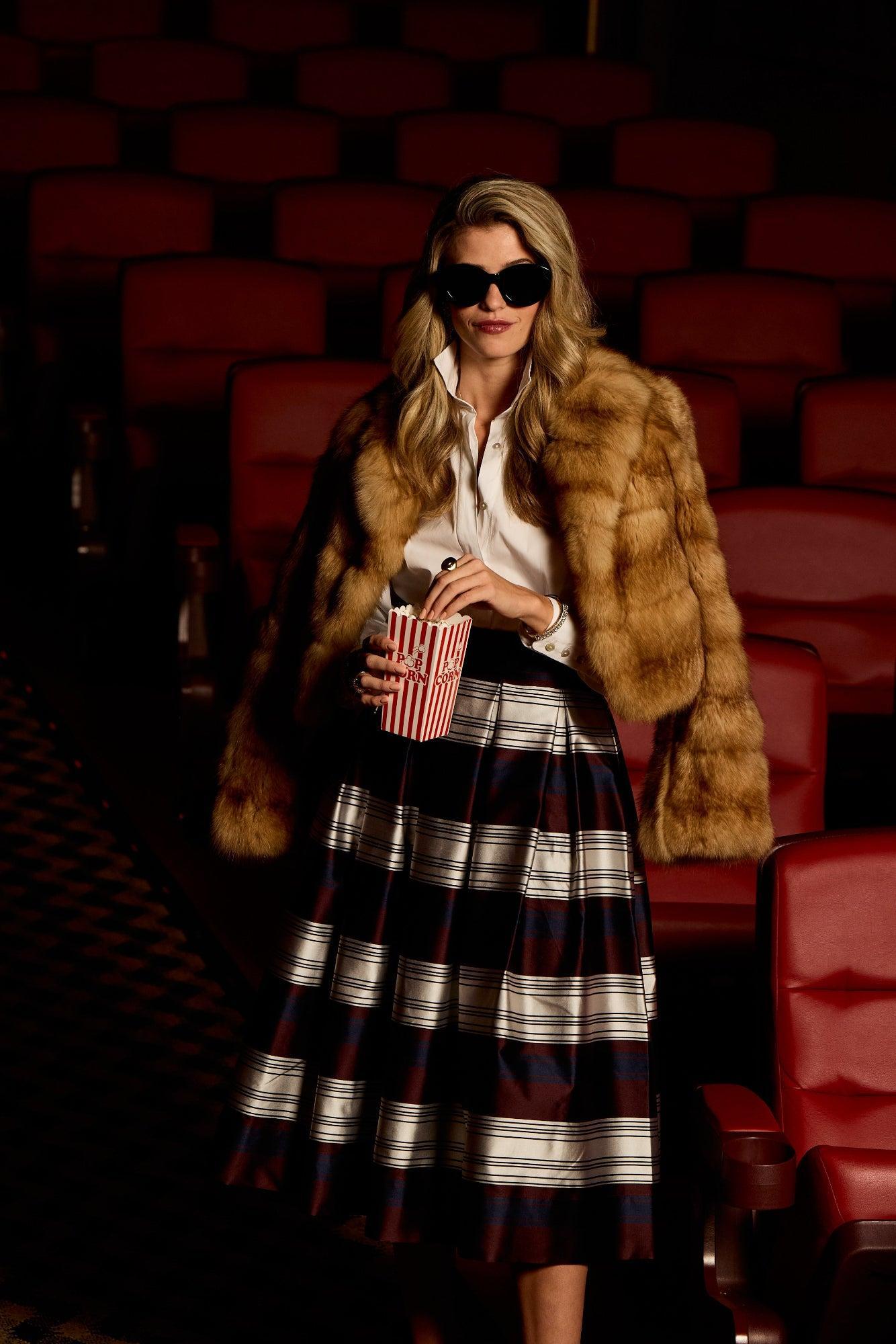 Woman in a fur coat and plaid skirt holding popcorn in a movie theater.