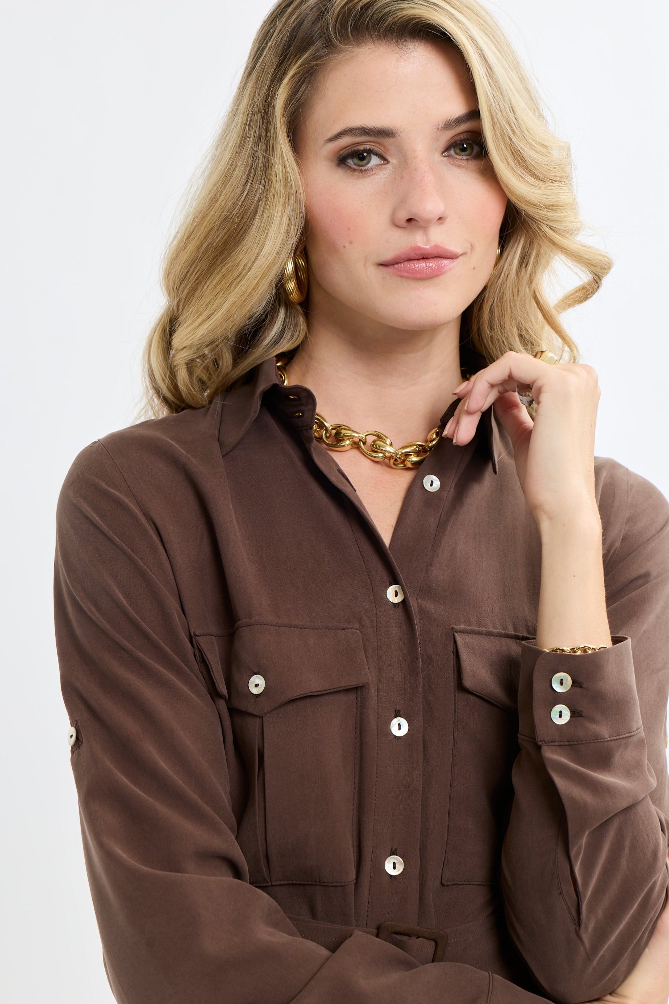 Woman wearing a brown shirt with a gold necklace on a white background