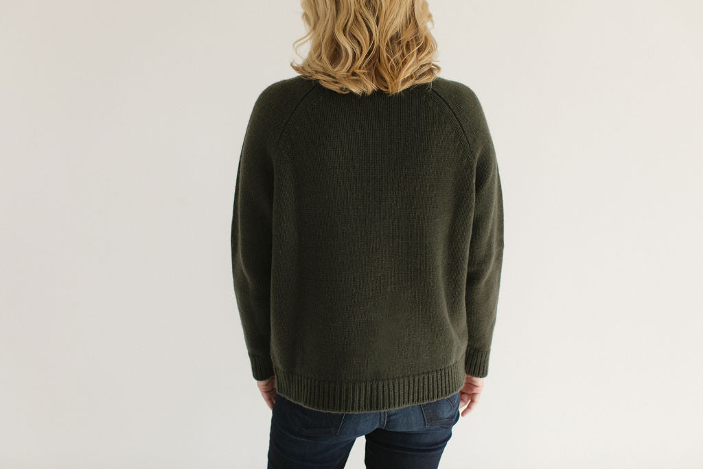 Back view of Eleanor Leftwich wearing the Forest Green Boyfriend Turtleneck, paired with dark jeans, against a white background.